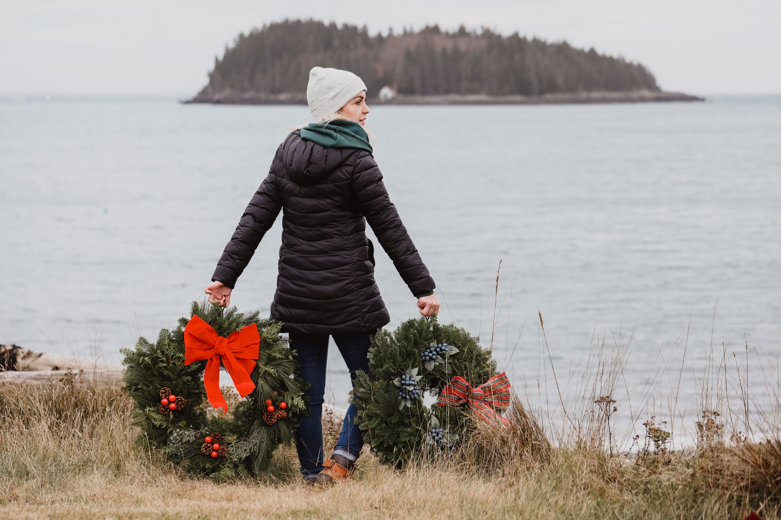 A woman holds two Whitney Wreaths by the ocean