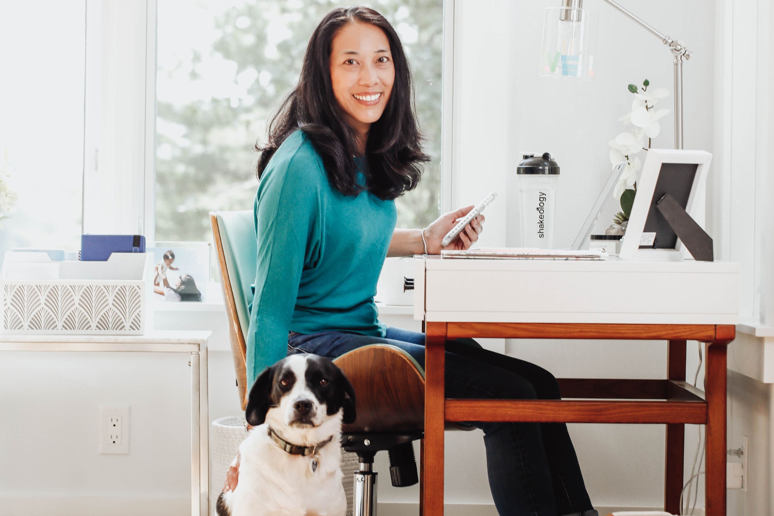 A woman sits at her home office desk and puts her hand on her dog
