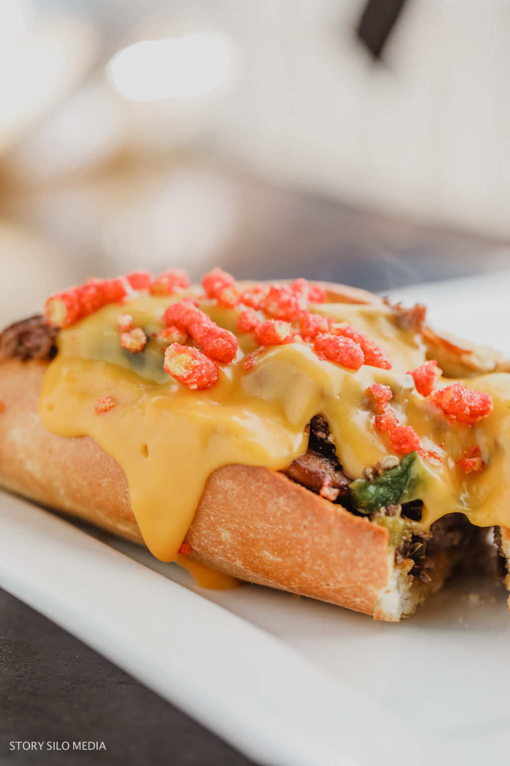 Image of a cheesesteak sandwich with cheese and Cheetos on it