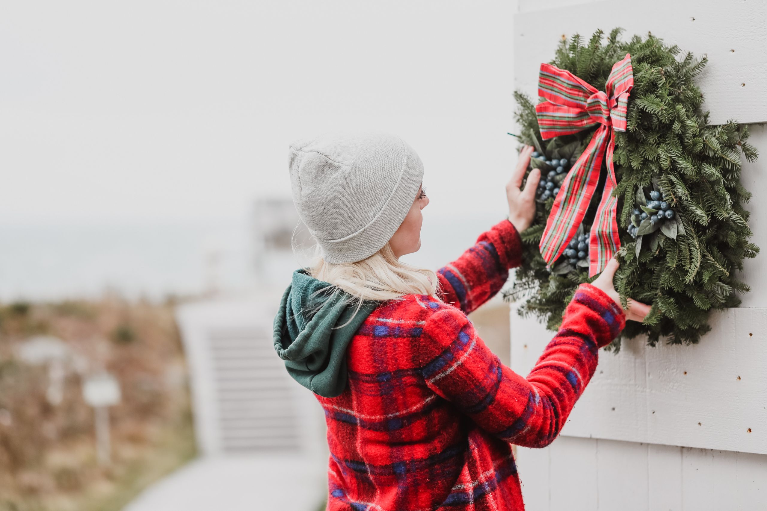 A woman hangs a Whitney's Christmas wreath on a house