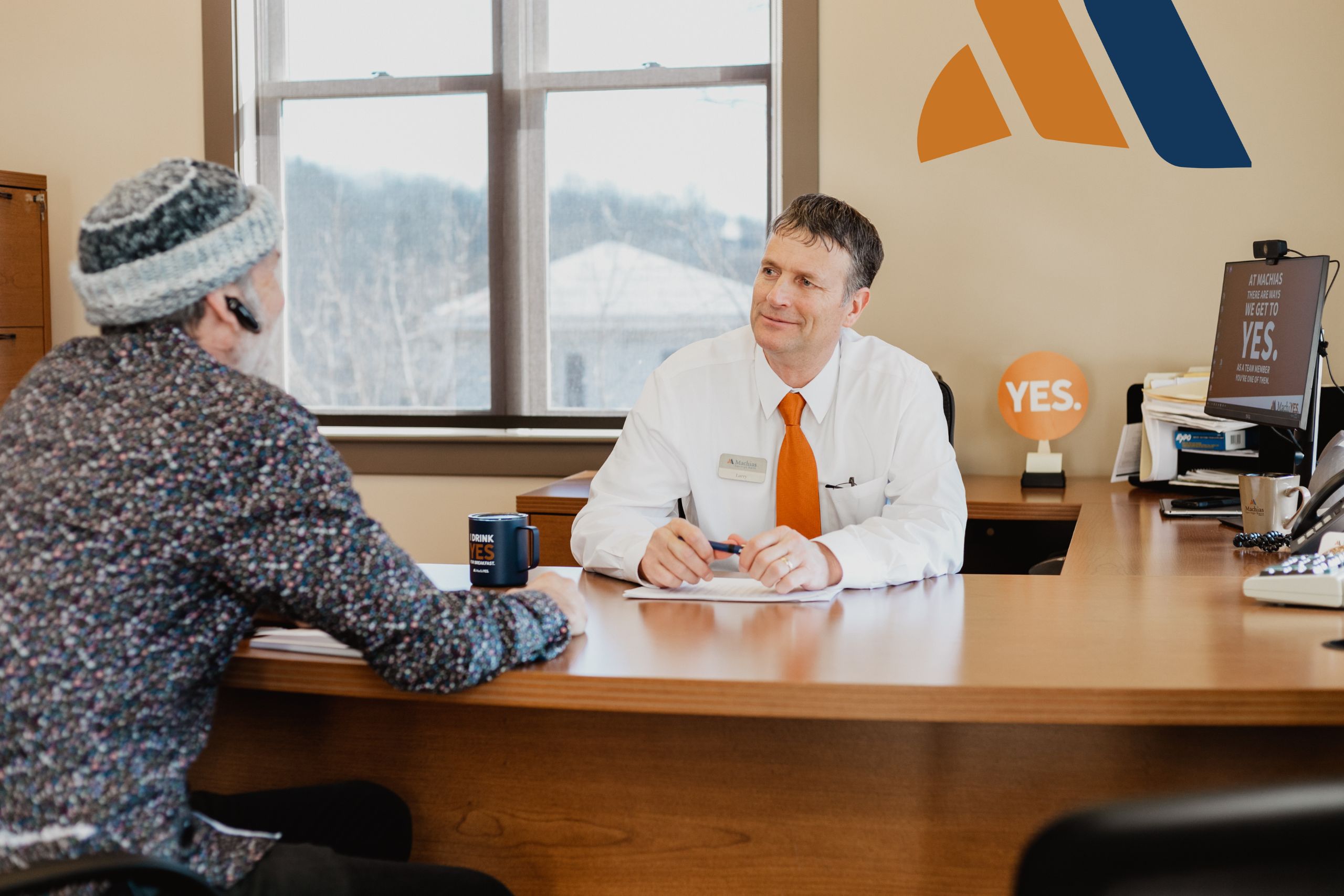 A Machias Savings Bank worker meets with a client. They are sitting in a office at a desk.