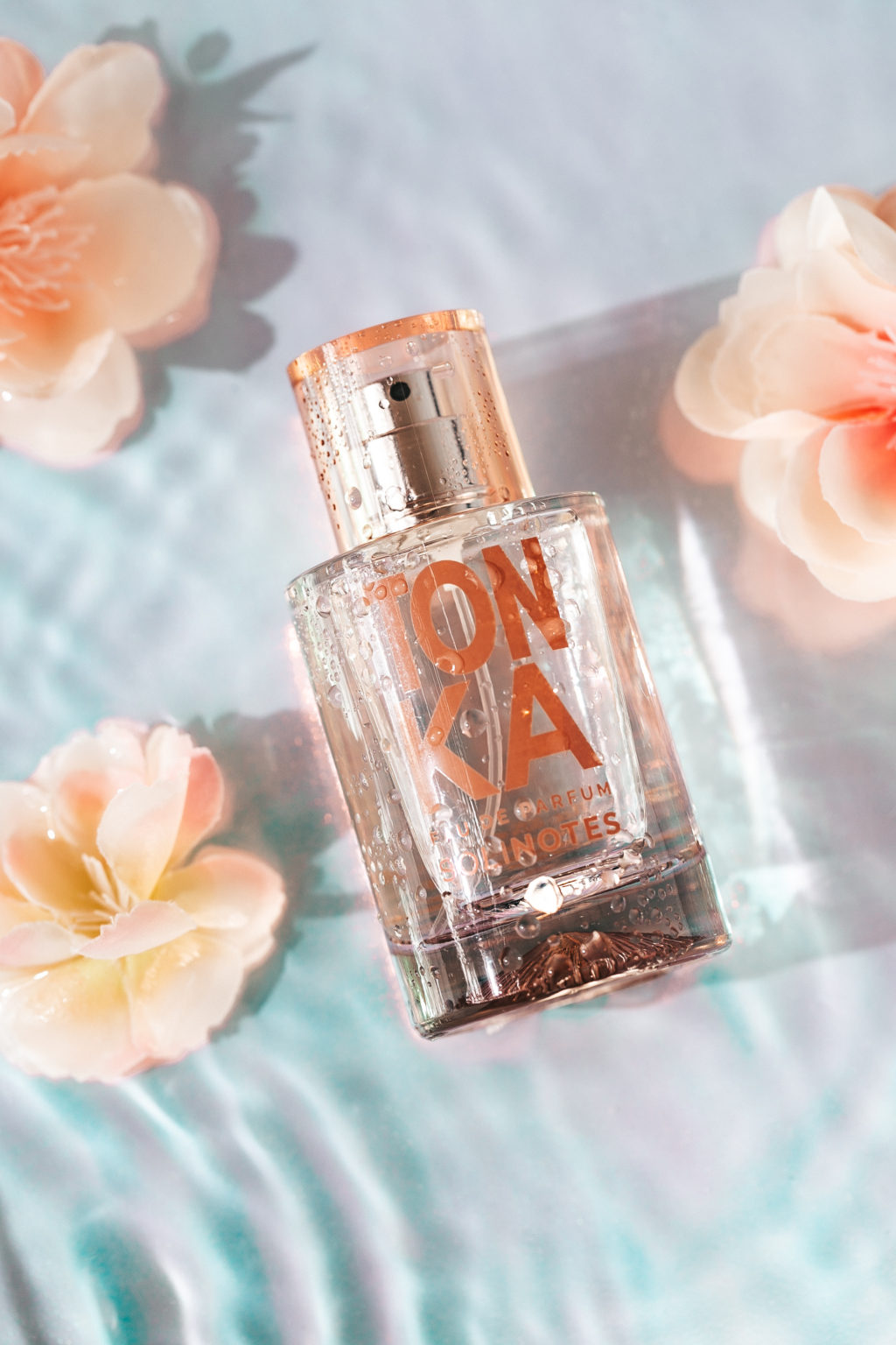 Image of Tonka perfume. Flowers are in the background and the bottle sits in shallow water